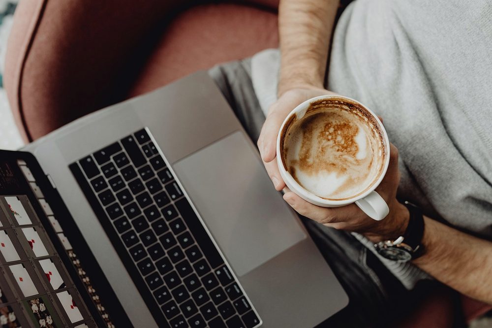 Hands holding a cup of coffee beside an open laptop